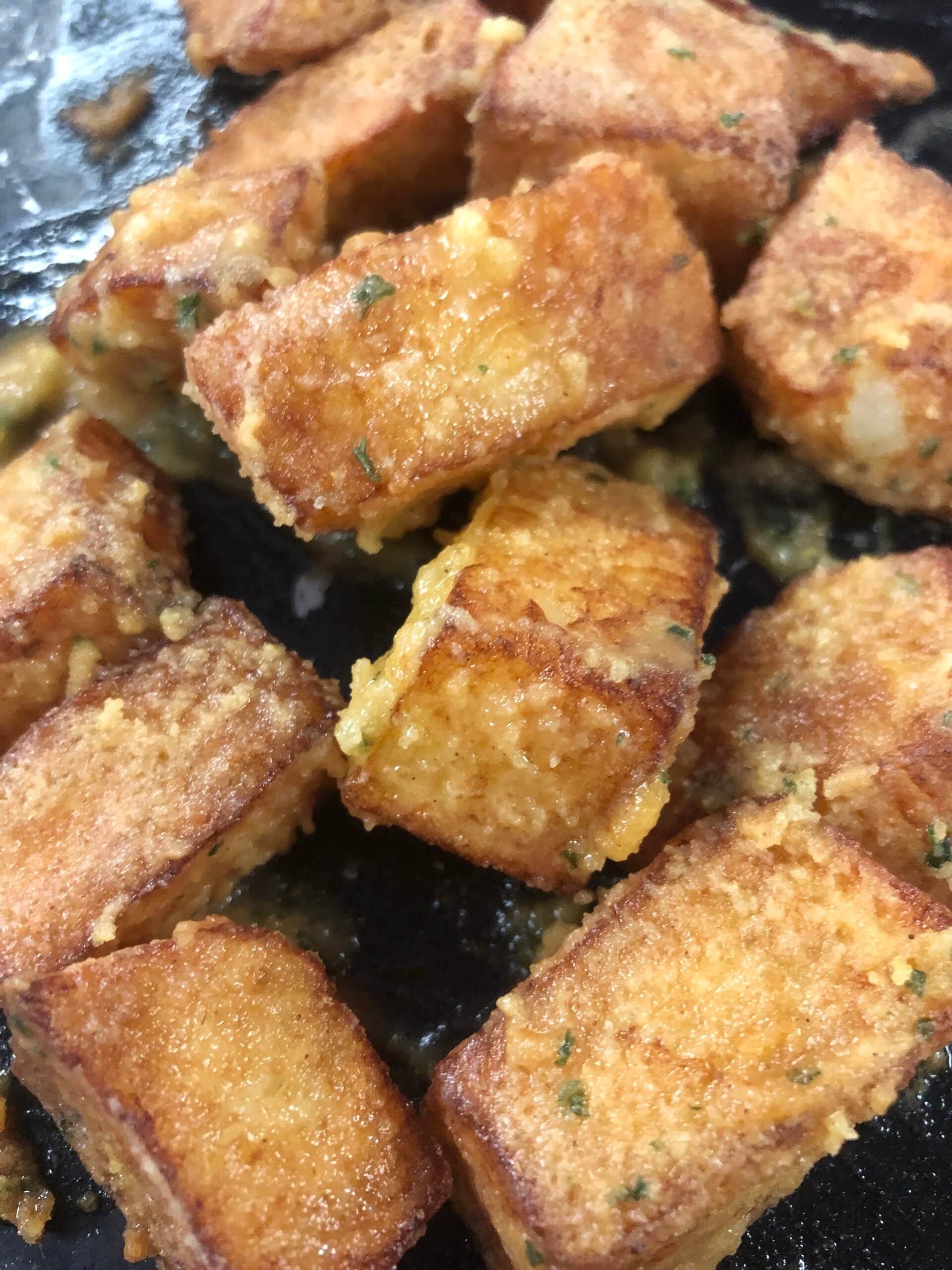 Cubes of fried cheese browning in a pan with herb butter