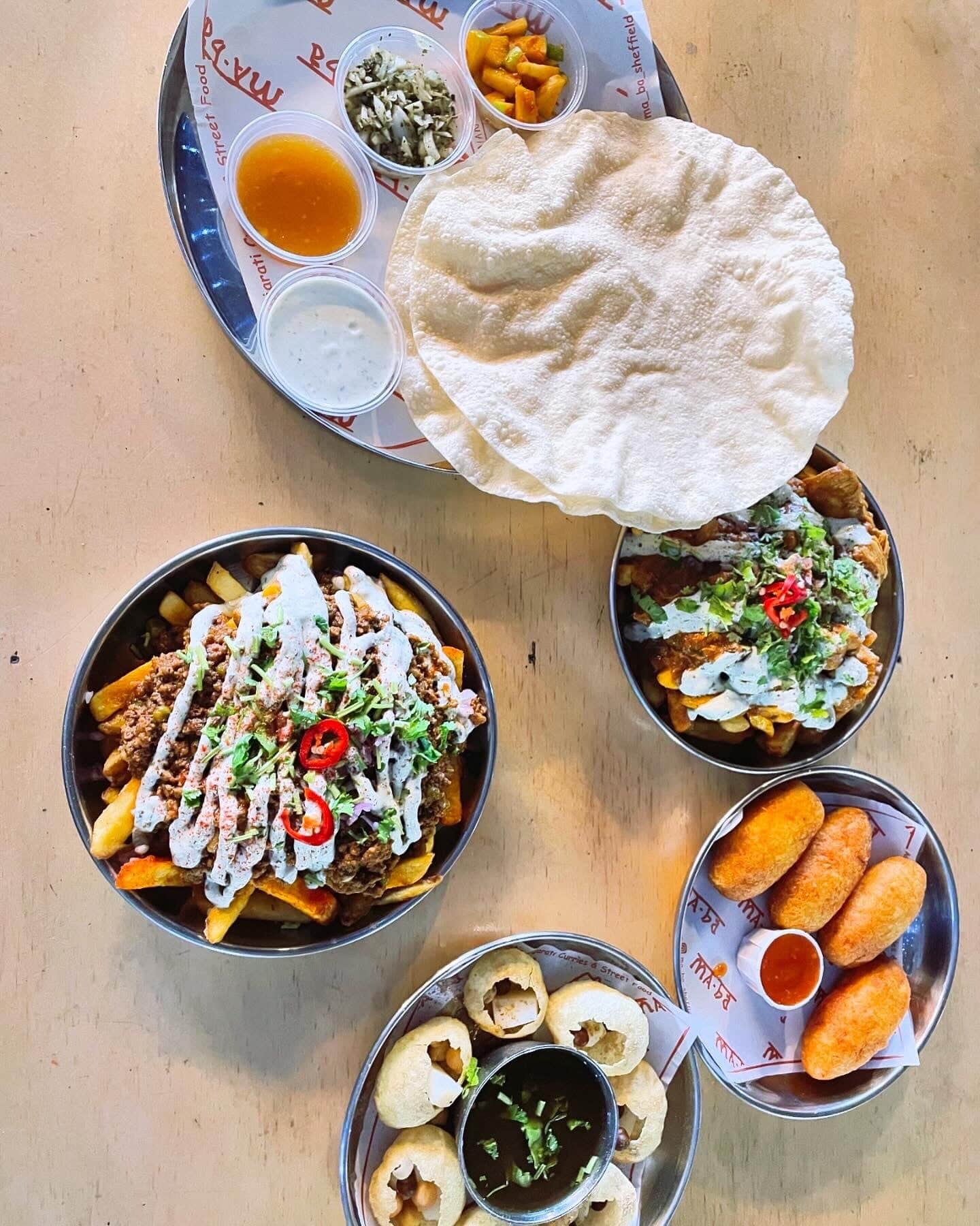 Steel trays of loaded fries, poppadoms, pani puri and croquettes on branded serving paper