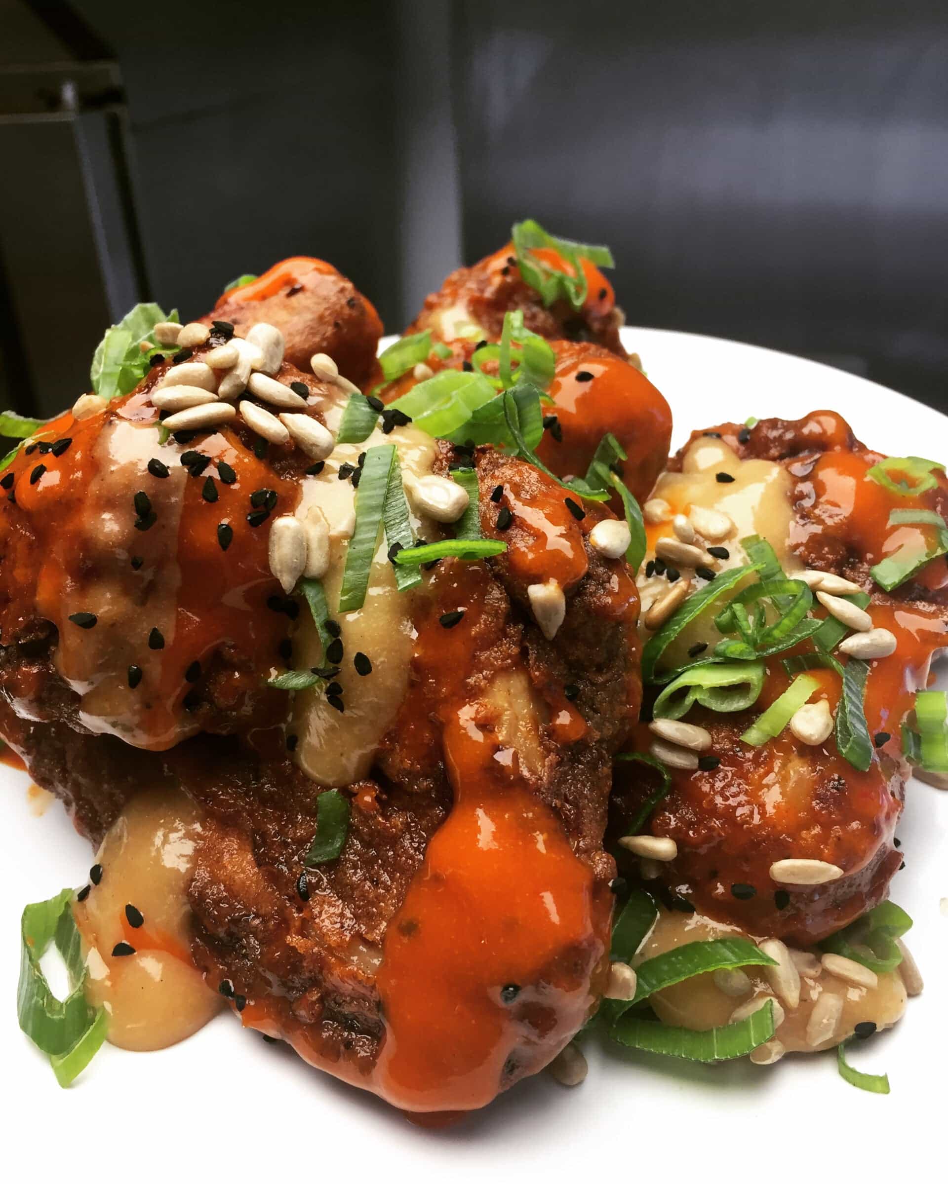 Asian buffalo chicken wings topped with spring onion and sesame seeds, plated in a kitchen